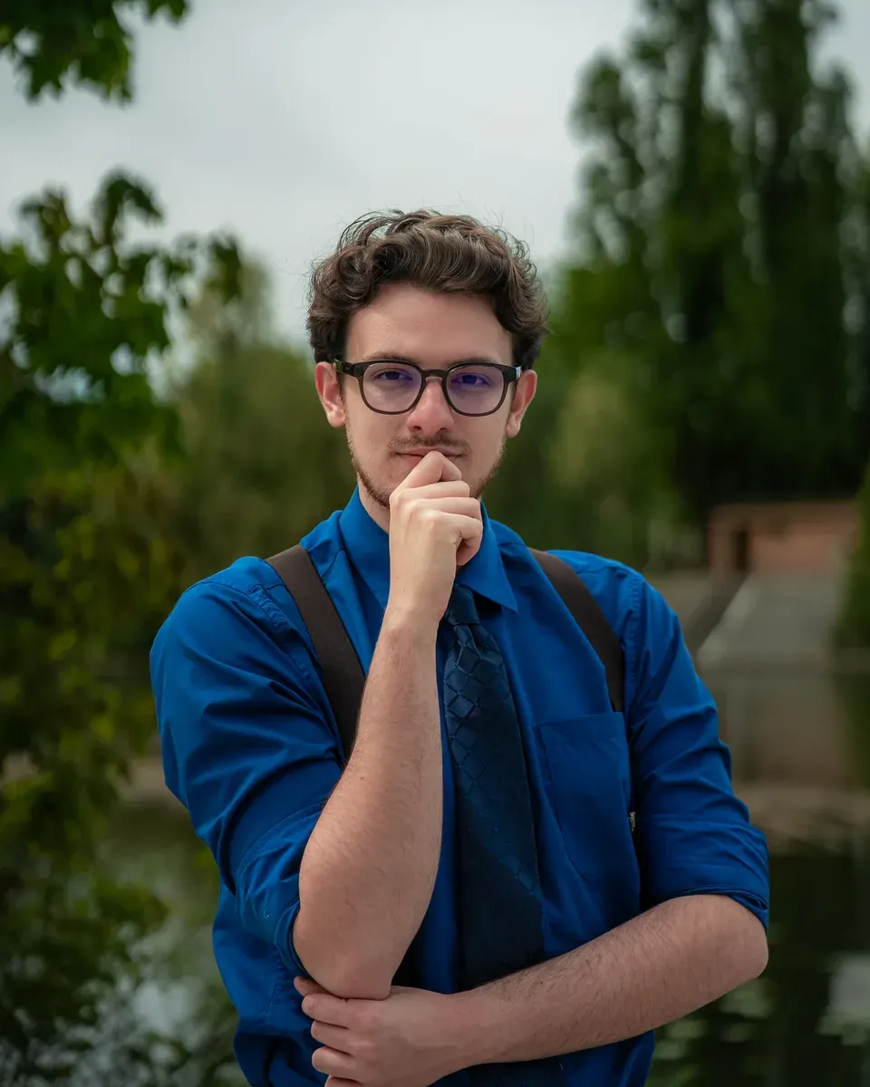 Charles Lindecker, en chemise bleu roi, la main au menton, devant un parc.